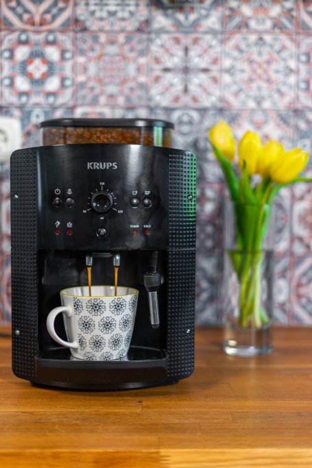 Schwarze Kaffeemaschine mit einer Tasse auf einem Tisch und einer Vase mit Tulpen.