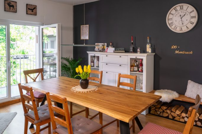 Heller Essbereich mit Holztisch, Stühlen, Pflanzen und einer Uhr an der Wand.