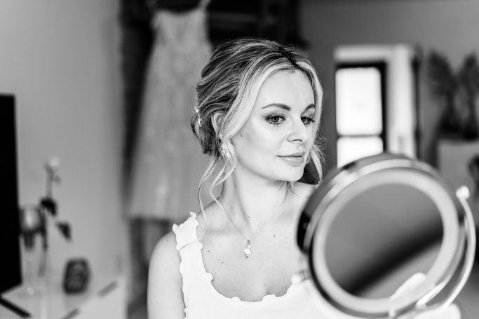 Frau mit Make-up, Blick in einen Schminkspiegel, Brautkleid im Hintergrund.