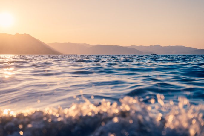 Sanfte Wellen im Meer bei Sonnenuntergang, mit goldenen Lichtreflexionen.