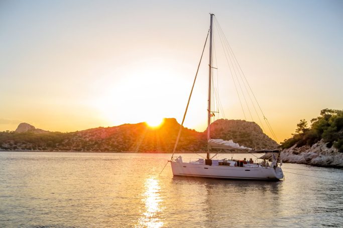 Segelyacht im Sonnenuntergang, umgeben von Bergen und ruhigem Wasser.