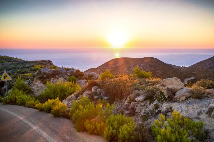 Sonnenuntergang über Hügel und Meer, umgeben von grüner Vegetation.