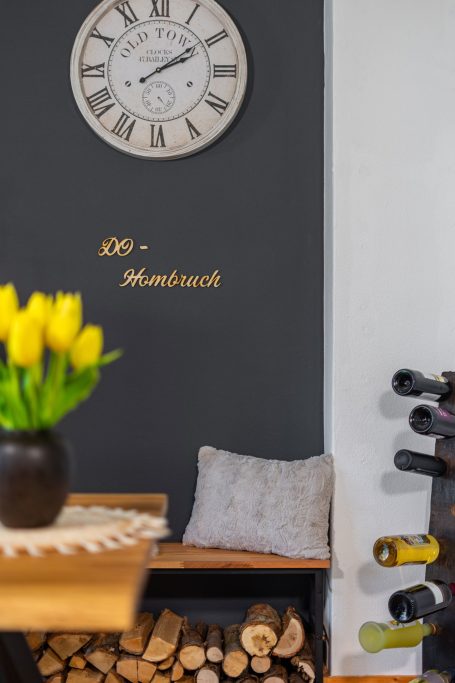 Wand mit einer Uhr, Blumenstrauß, Holzlager und Weinständer.