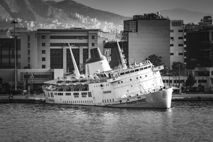 Ein verfallenes Schiff liegt schräg im Wasser vor einer städtischen Kulisse.